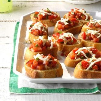 small appetizers with tomatoes and cheese on a white platter next to a green napkin