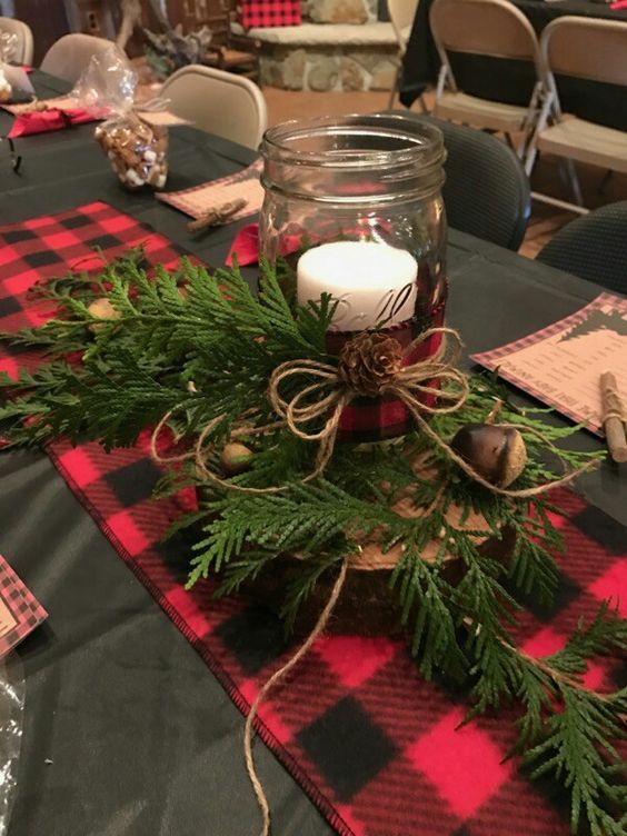 a jar filled with candles sitting on top of a table covered in greenery and pine cones