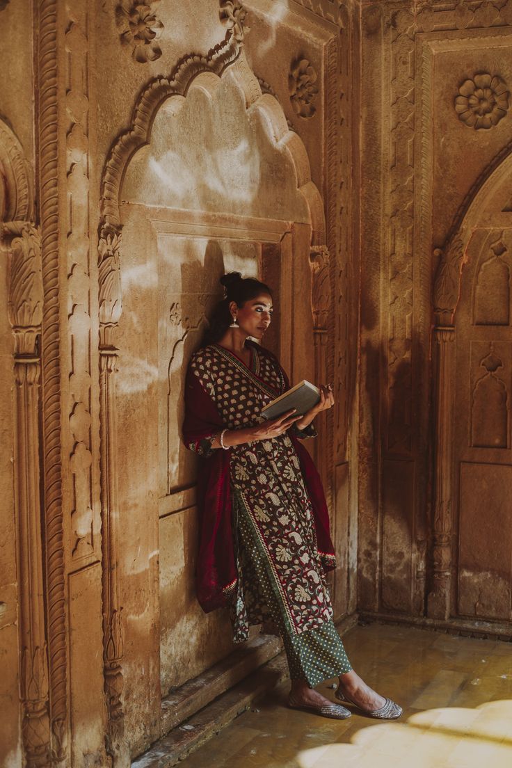 a woman standing next to a wall holding a book in one hand and looking at the other