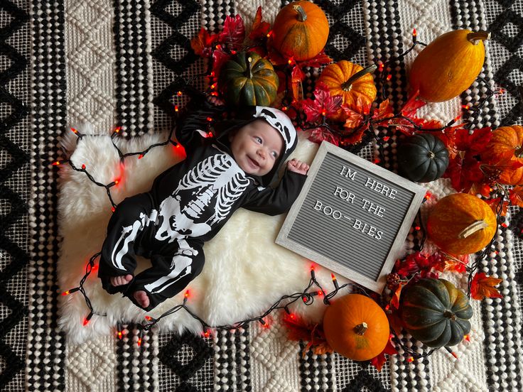 a baby is laying on a rug next to pumpkins and other decorations with a sign that says, i'm here for the boosies