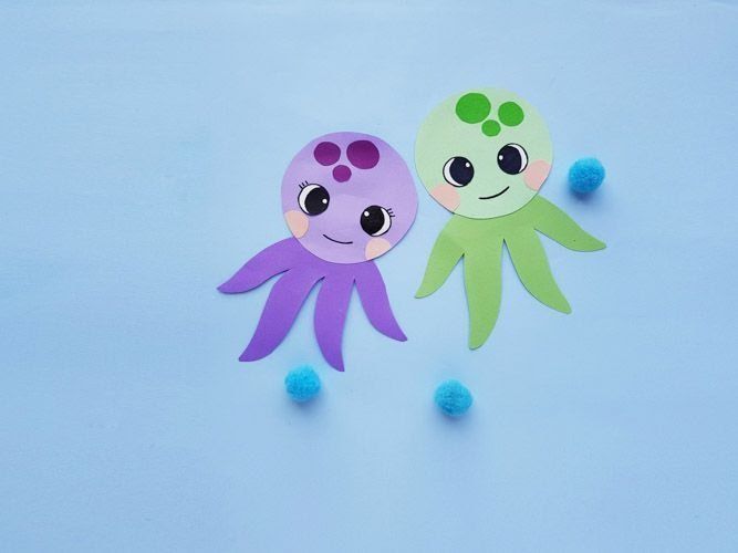 two paper cut outs with faces and eyes sitting on top of each other next to blue pom poms