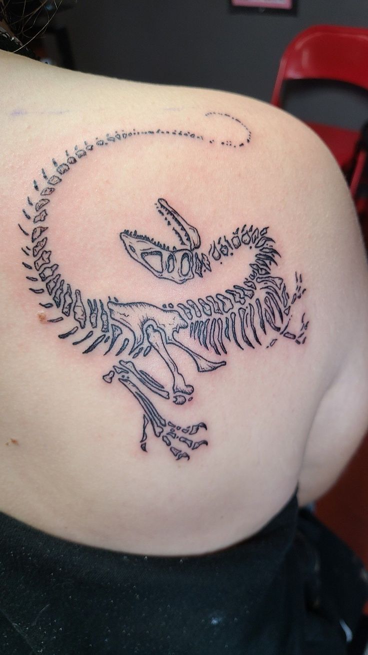 the back of a woman's shoulder with a tattoo of a dinosaur skeleton on it