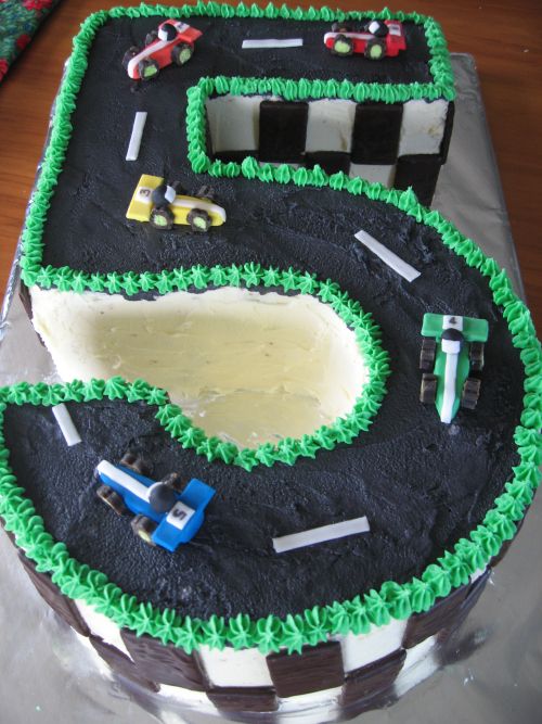 a birthday cake that is shaped like a race track with cars and trucks on it