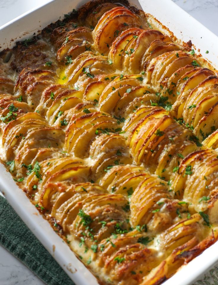 a casserole dish with potatoes and parsley in it on a marble table