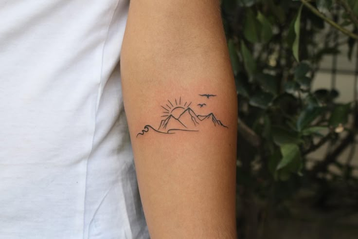 a man with a tattoo on his arm that has mountains and birds in the sky