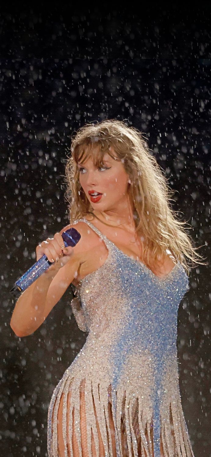 a woman in a white dress holding a blue bottle while standing on stage with snow falling all around her