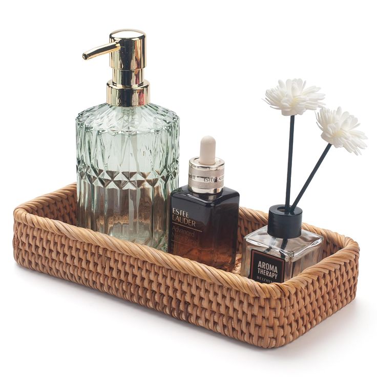 a basket with some bottles and flowers in it on a white surface, next to a bottle of cologne