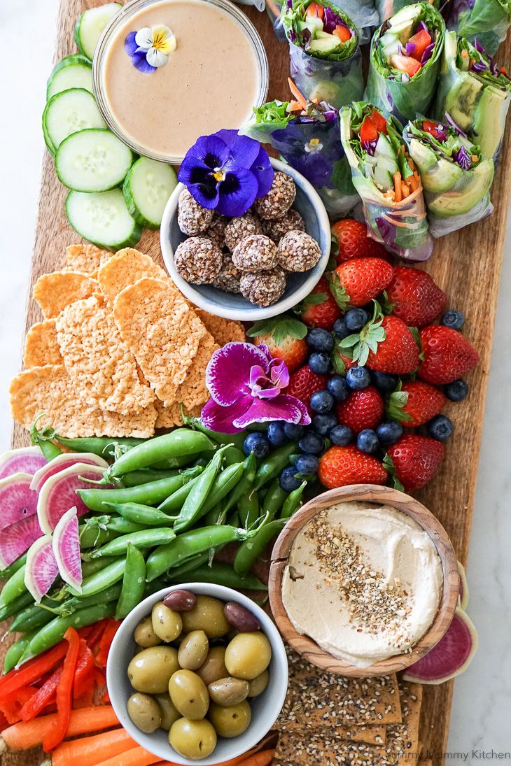 an assortment of fruits, vegetables and dips on a cutting board with crackers