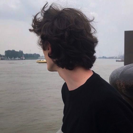 a man with curly hair looking out over the water from a boat in the distance