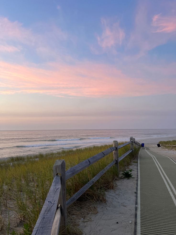 a wooden fence on the side of a road next to an empty beach at sunset