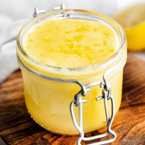 a glass jar filled with yellow liquid sitting on top of a wooden table next to sliced lemons