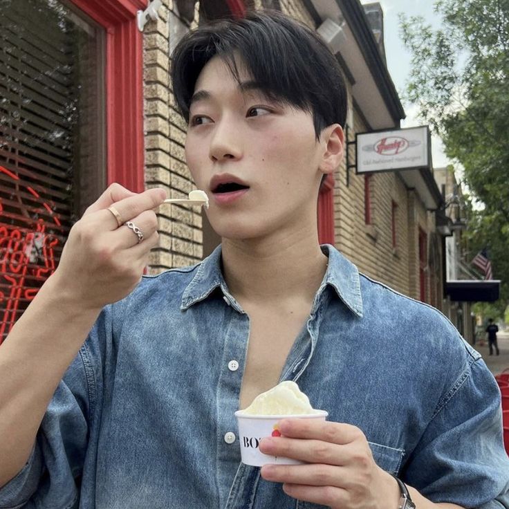 a young man eating ice cream from a paper cup in front of a red door