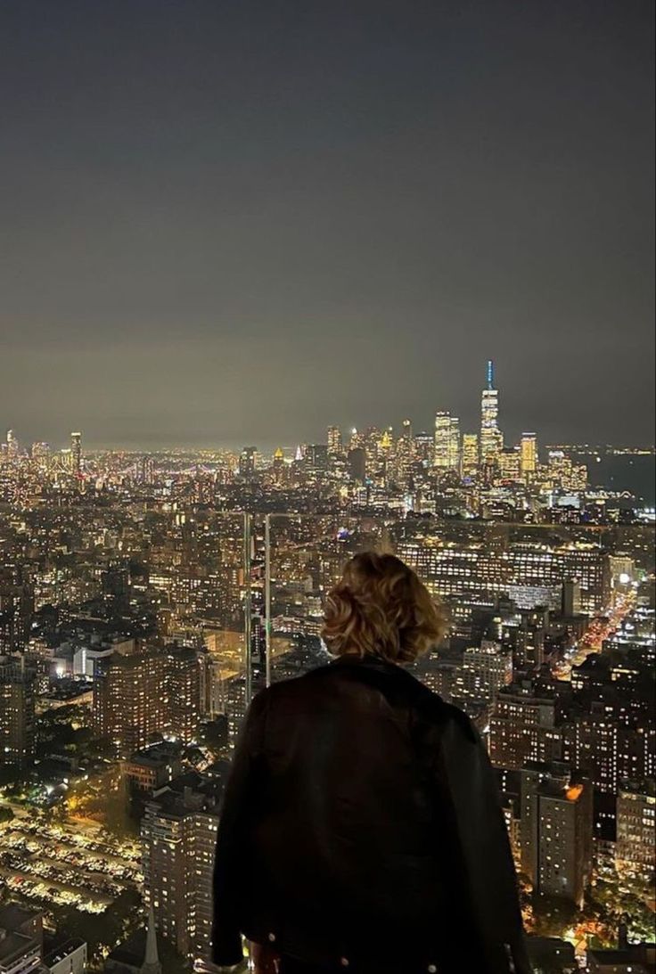 a person standing on top of a tall building looking at the city lights in the distance