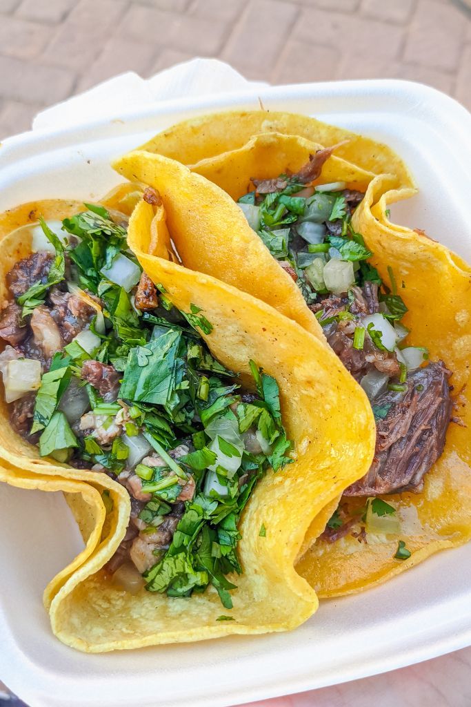 two tortillas with meat and greens in a white container on a table outside