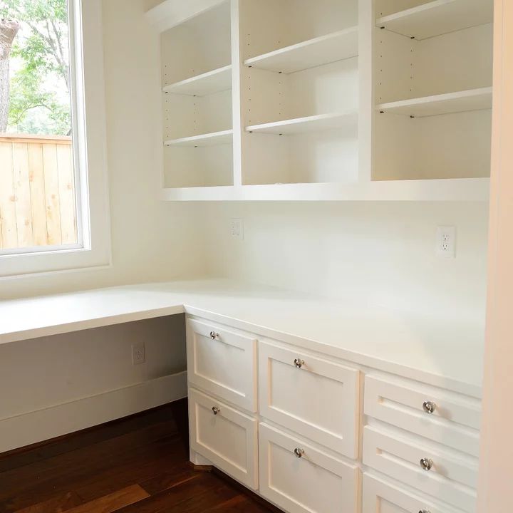 an empty room with white cupboards and shelves on the wall next to a window