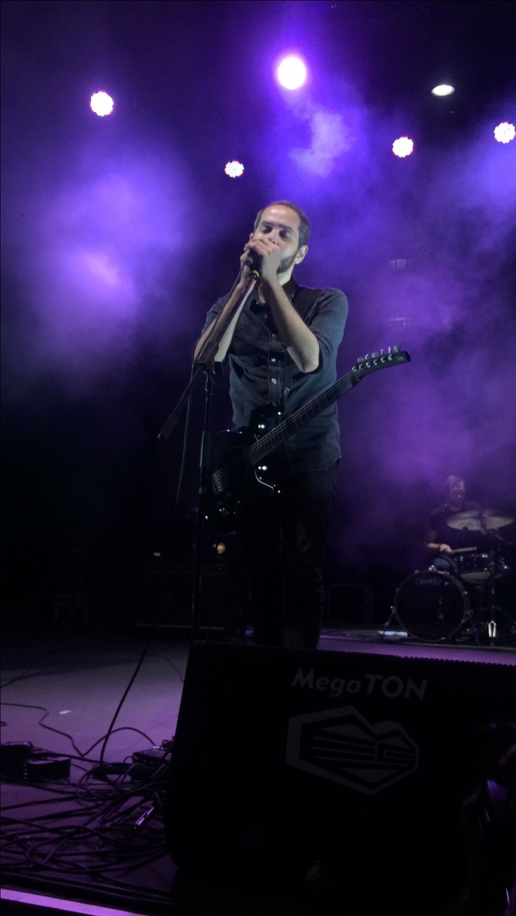 a man singing into a microphone while standing in front of a stage with purple lights