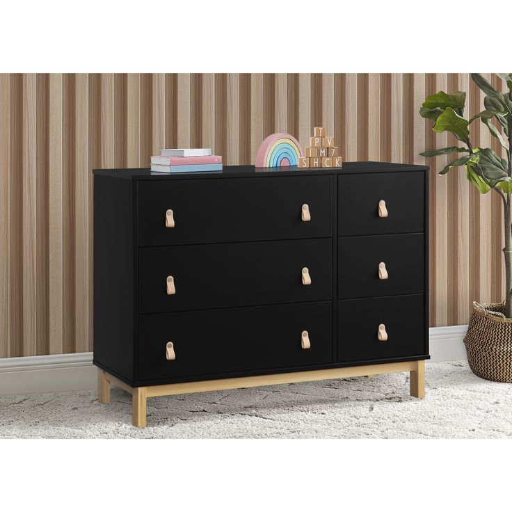 a black dresser with gold handles in front of a striped wallpapered area and a potted plant