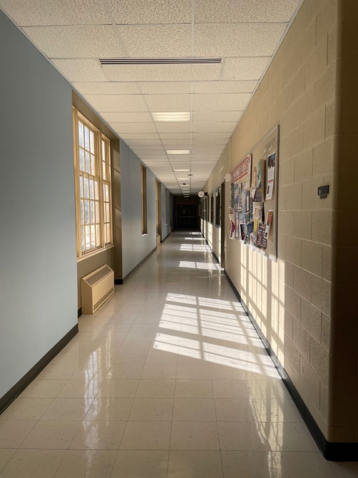 an empty hallway with posters on the wall and windows in the middle is seen from across the room