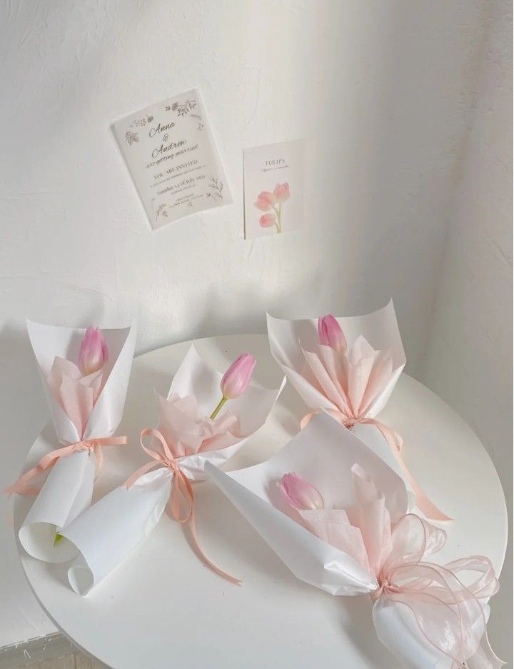 three pink flowers are sitting on a white table with some paper wrapped around them and tied together