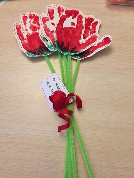 three red flowers with green stems on a wooden table next to markers and pencils