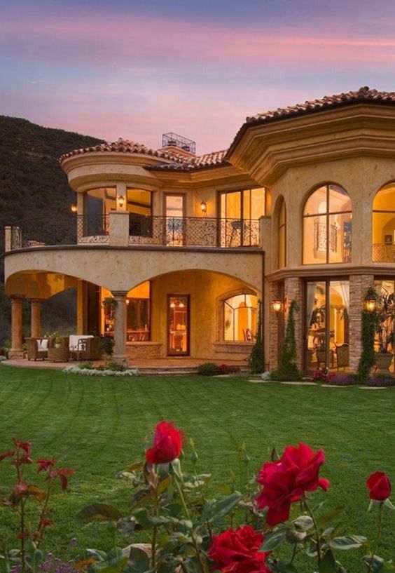 a large house with lots of windows and flowers in the front yard at night time