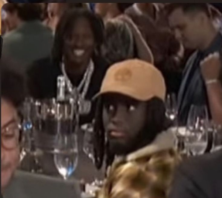 two men sitting at a table with wine glasses in front of them and one man wearing a hat