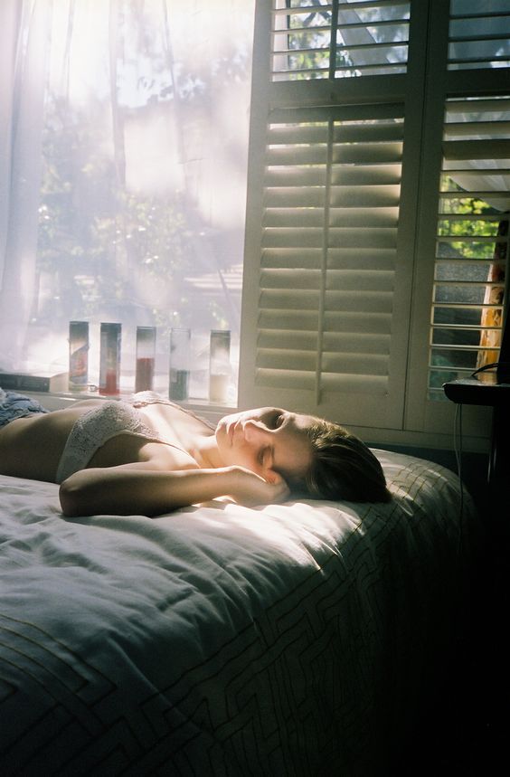 a woman laying on top of a bed in a bedroom next to a window with shutters