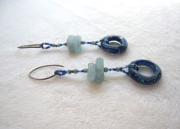 These ocean colored stones will give off some serious mermaid vibes! Like the sea itself, this pair of earrings is fluid! They can easily be worn with day or night looks. Radiant hand made glass rings suspend below exquisite aquamarine stones. Sterling silver ear wires. 2 1/2" long. Elegant Recycled Glass Earrings With Ear Wire, Blue Adjustable Long Drop Jewelry, Ocean-inspired Blue Earrings With Ear Wire, Nickel Free Blue Aquamarine Earrings, Handmade Light Blue Aquamarine Jewelry, Nickel-free Blue Aquamarine Jewelry, Blue Aquamarine Nickel-free Earrings, Blue Aquamarine Earrings Nickel Free, Blue Glass Wire Wrapped Earrings