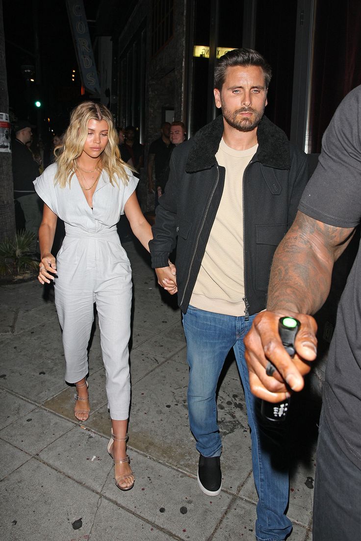 a man and woman holding hands while walking down the street at night with other people