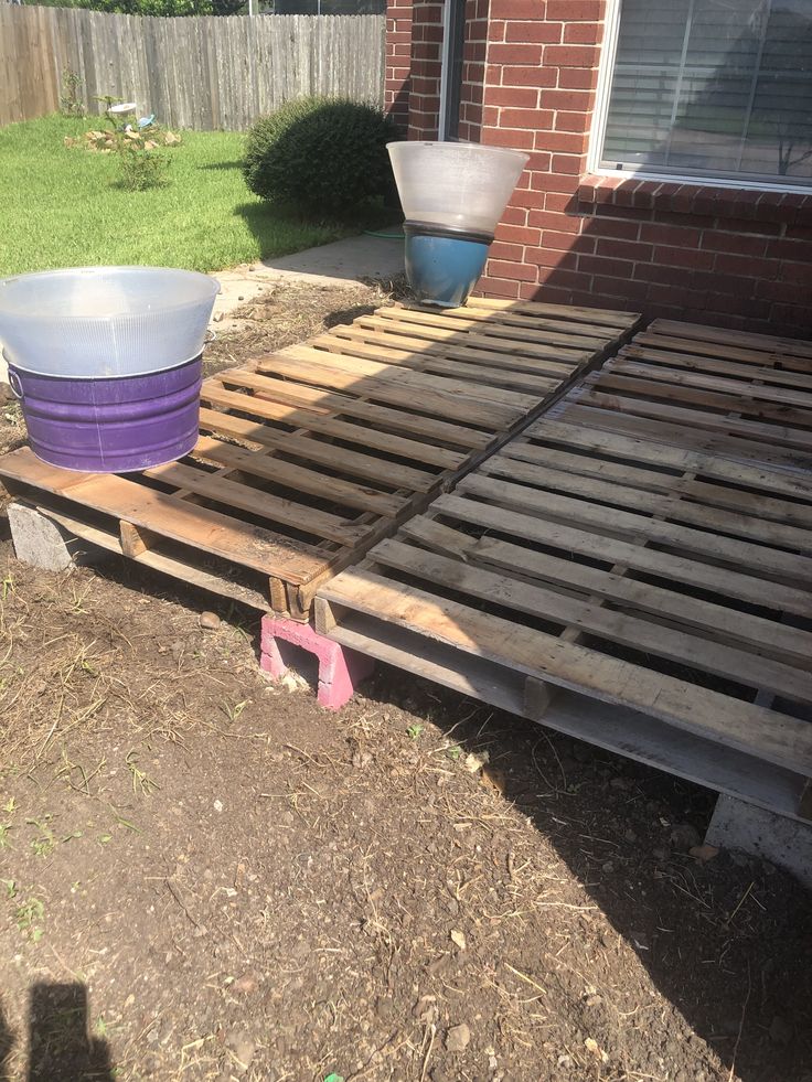 a bed frame made out of pallet wood and some buckets on the ground