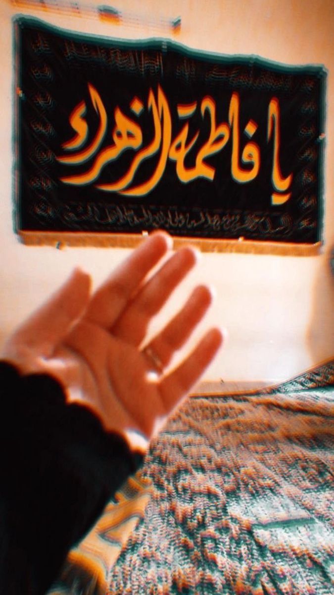 a person holding their hand up in front of a sign with arabic writing on it