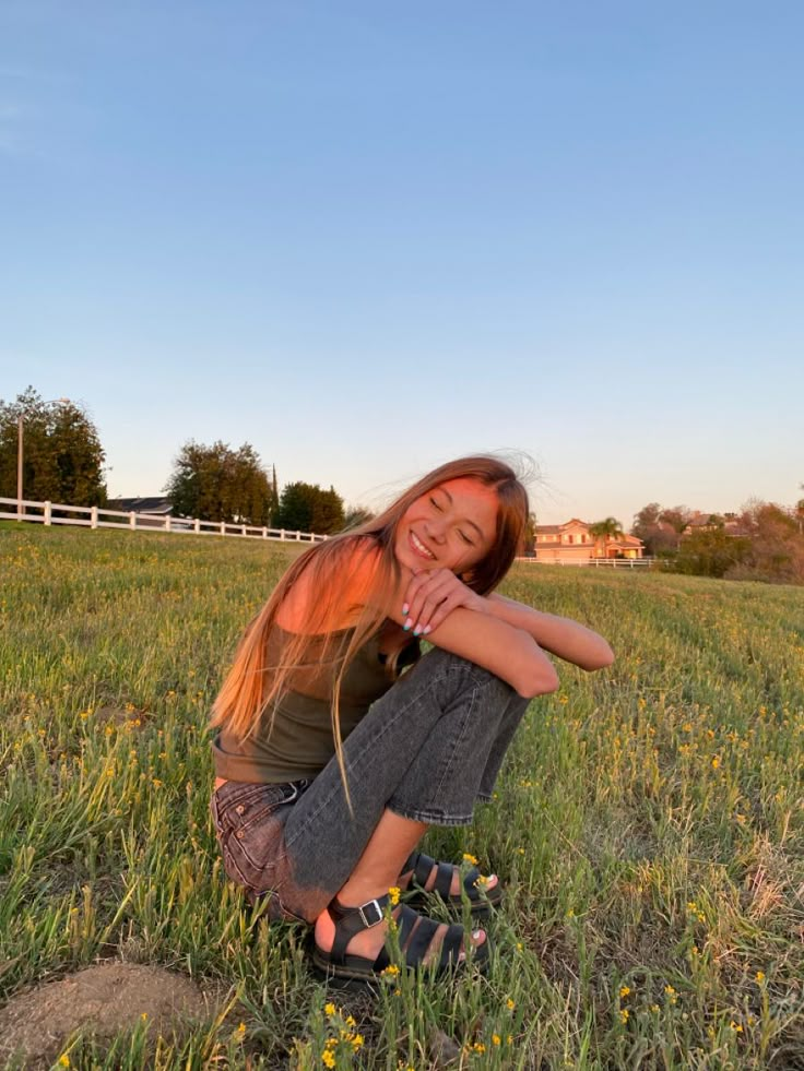 a woman sitting in the grass with her arms crossed