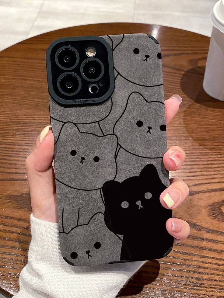 a woman is holding up her phone case with cats on it and coffee cup in the background