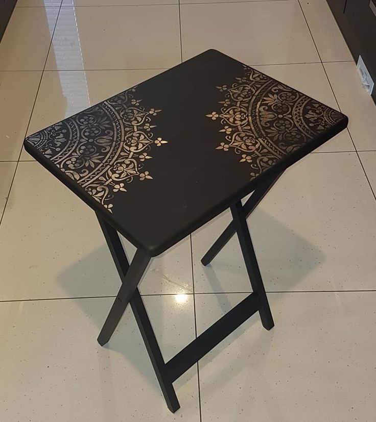 a small black table with gold designs on the top and bottom, sitting on a tiled floor