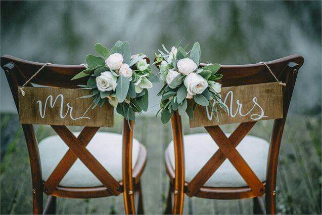 two wooden chairs with white flowers and mr and mrs signs on the back of them