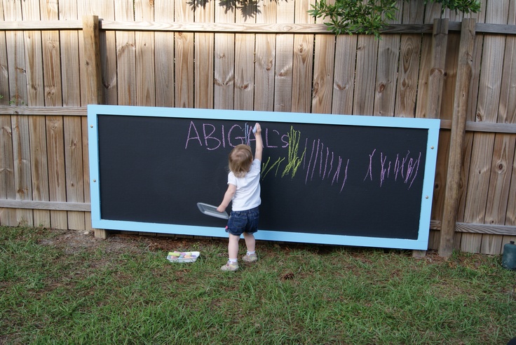 a little boy writing on a chalkboard in front of a fence