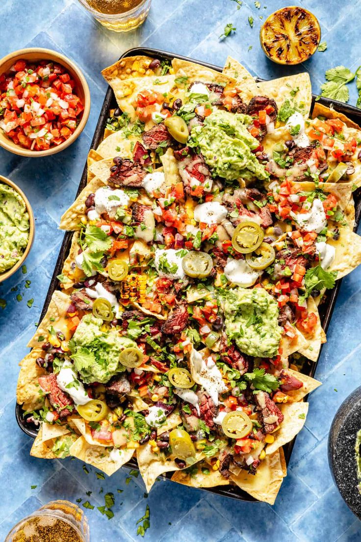 nachos with guacamole, tomatoes and other toppings on a tray