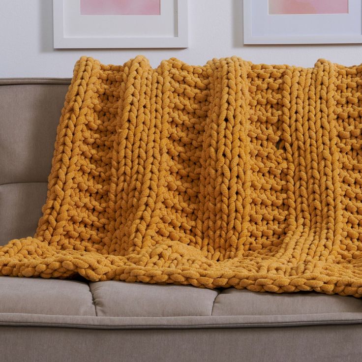 a yellow knitted blanket sitting on top of a couch next to two framed pictures