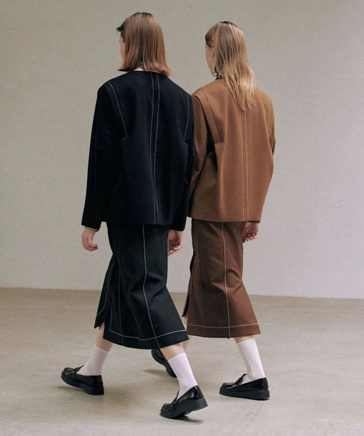 two women in black and brown outfits are walking side by side with one woman's back to the camera