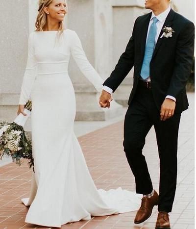 a bride and groom holding hands while walking down the street in front of a building