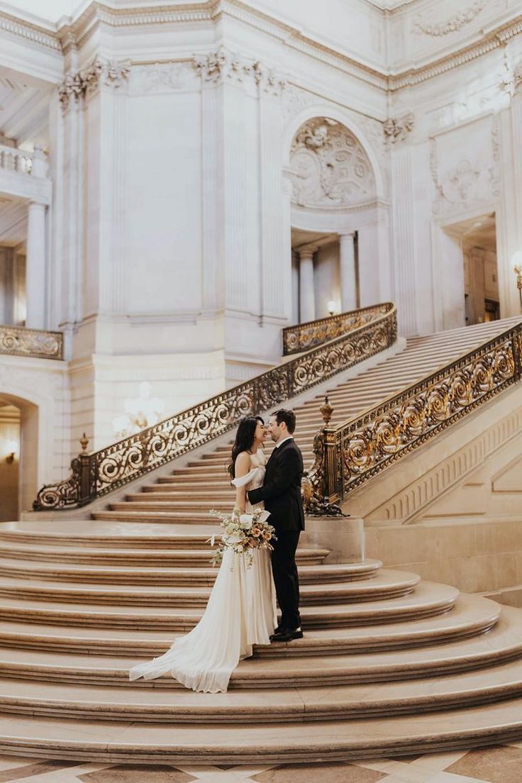 a bride and groom standing on the steps of a grand staircase in an ornate building