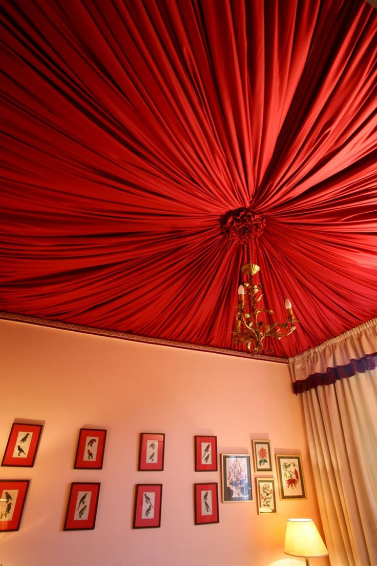 the ceiling is covered with red drapes and pictures on the wall above it, along with a chandelier