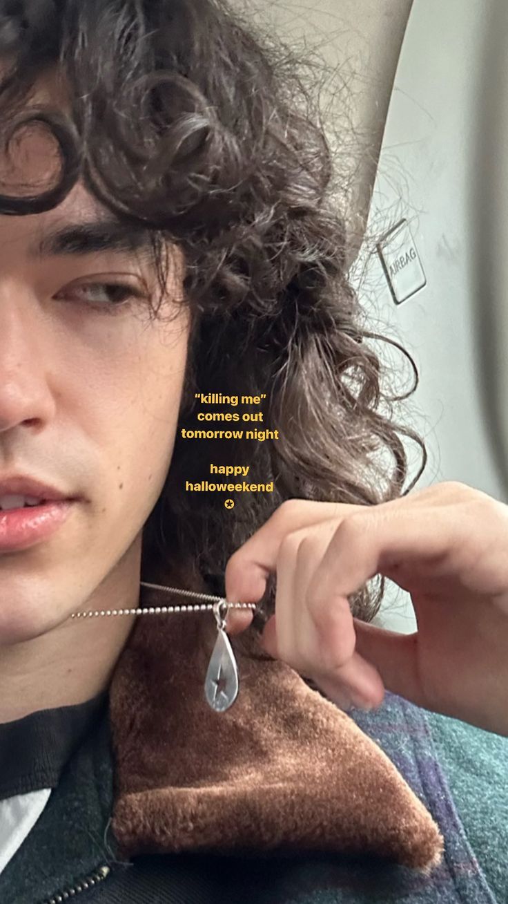 a young man with curly hair wearing a jacket and holding a necklace in his left hand