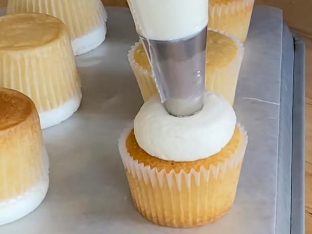 some cupcakes with icing being made on top of each other in front of them