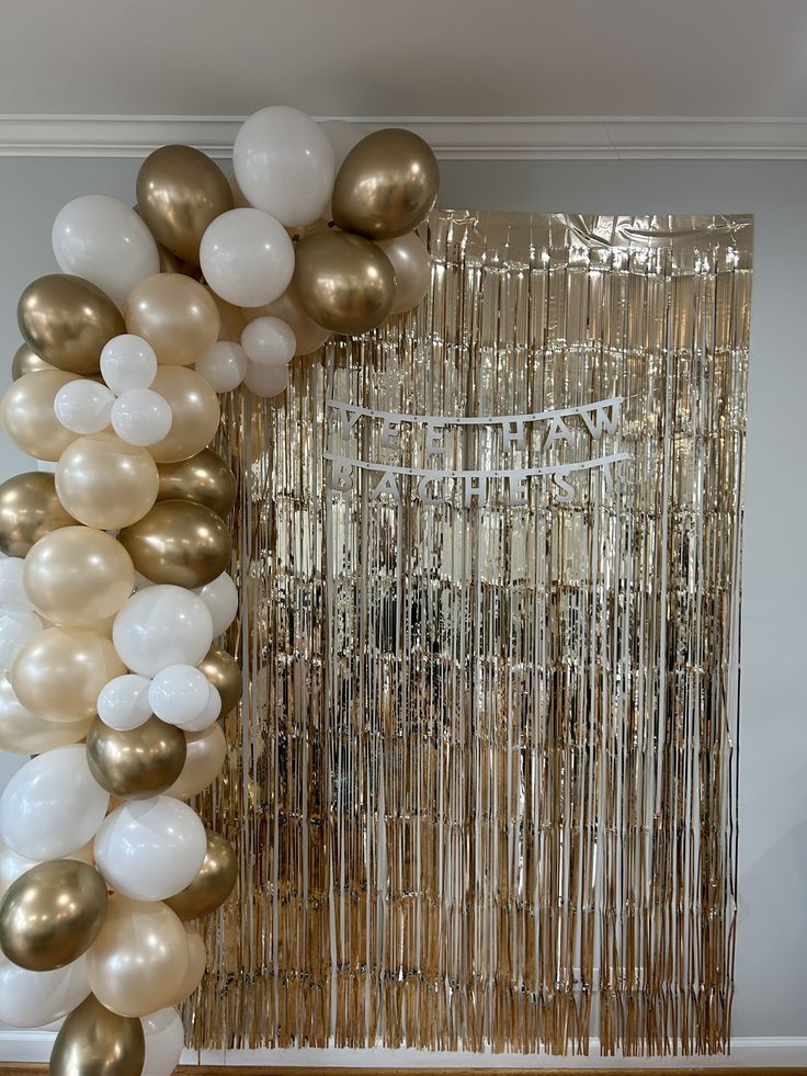 gold and white balloons are hanging from the ceiling in front of a large balloon arch