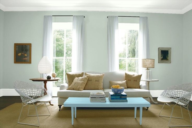 a living room with green walls, white furniture and two large windows in the corner