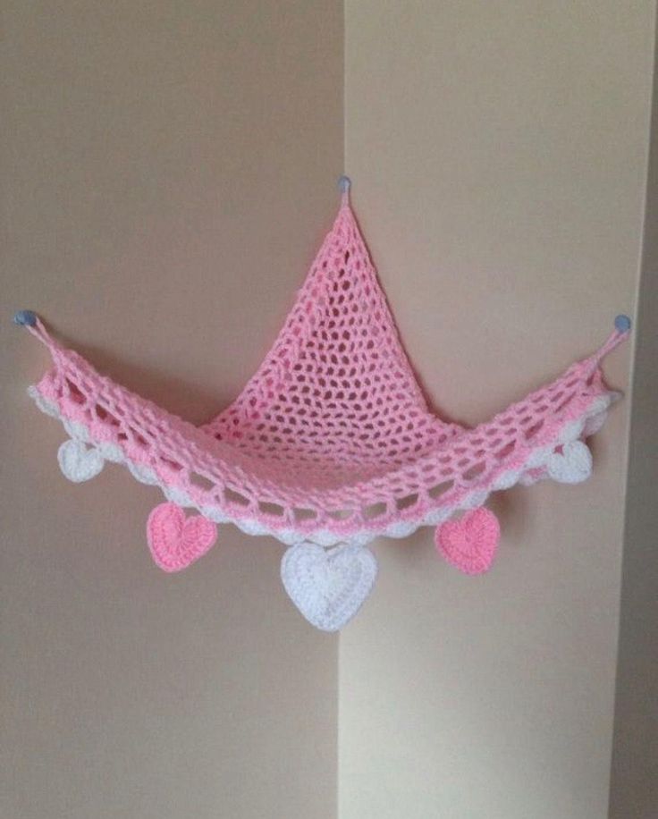 a pink crocheted hammock hanging from the wall with hearts on it