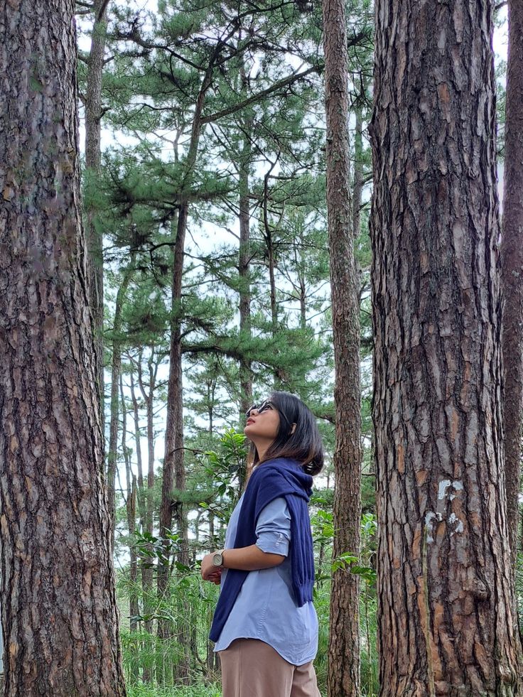 a woman standing in the woods looking up into the sky