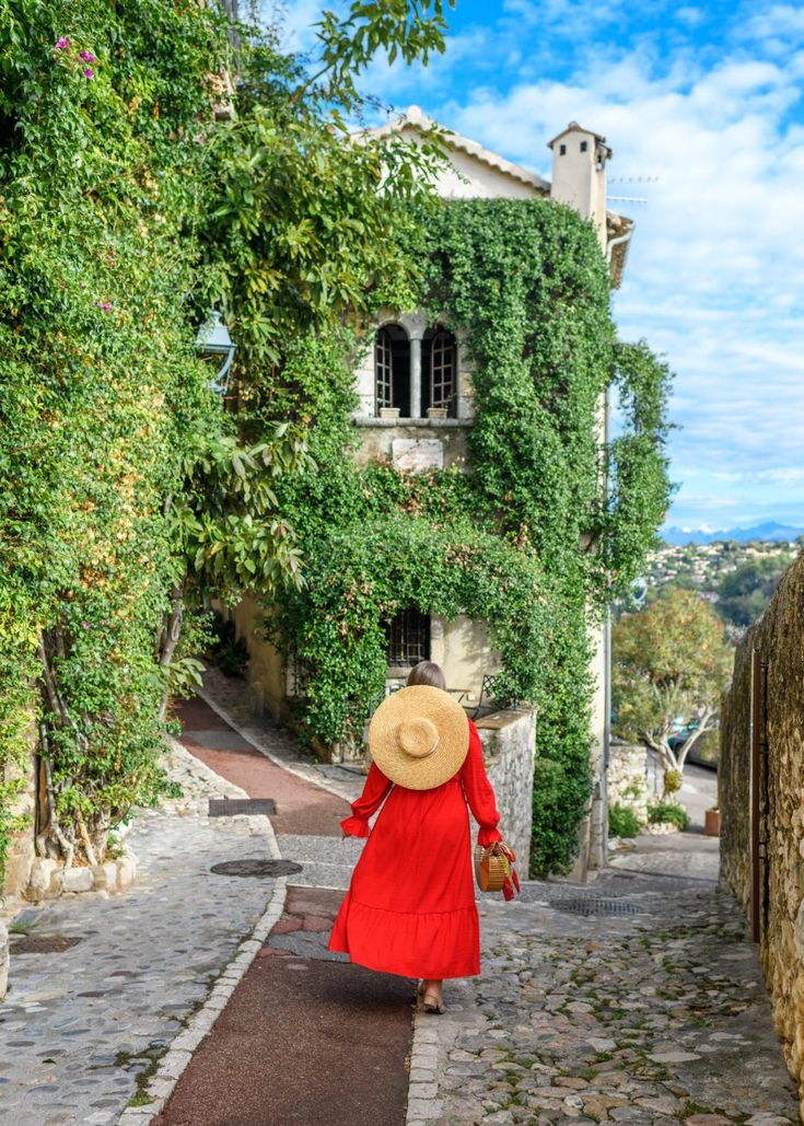 a woman in a red dress and straw hat walking down a cobblestone street