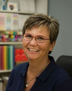 a woman with glasses sitting in front of a book shelf and smiling at the camera